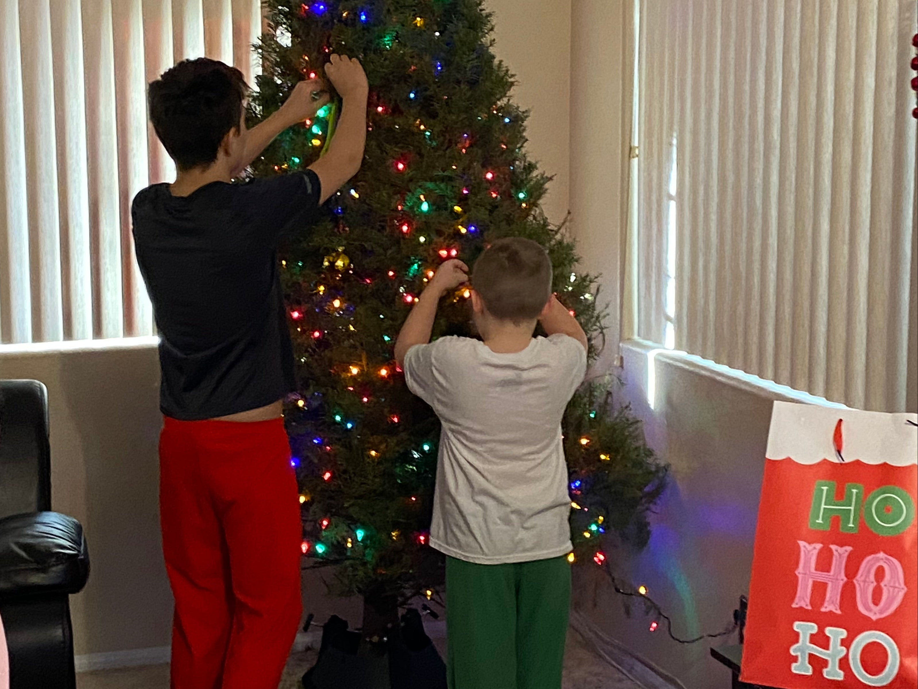 Two children upside down on a Christmas tree with a person looking up at them, in a room decorated for Christmas.